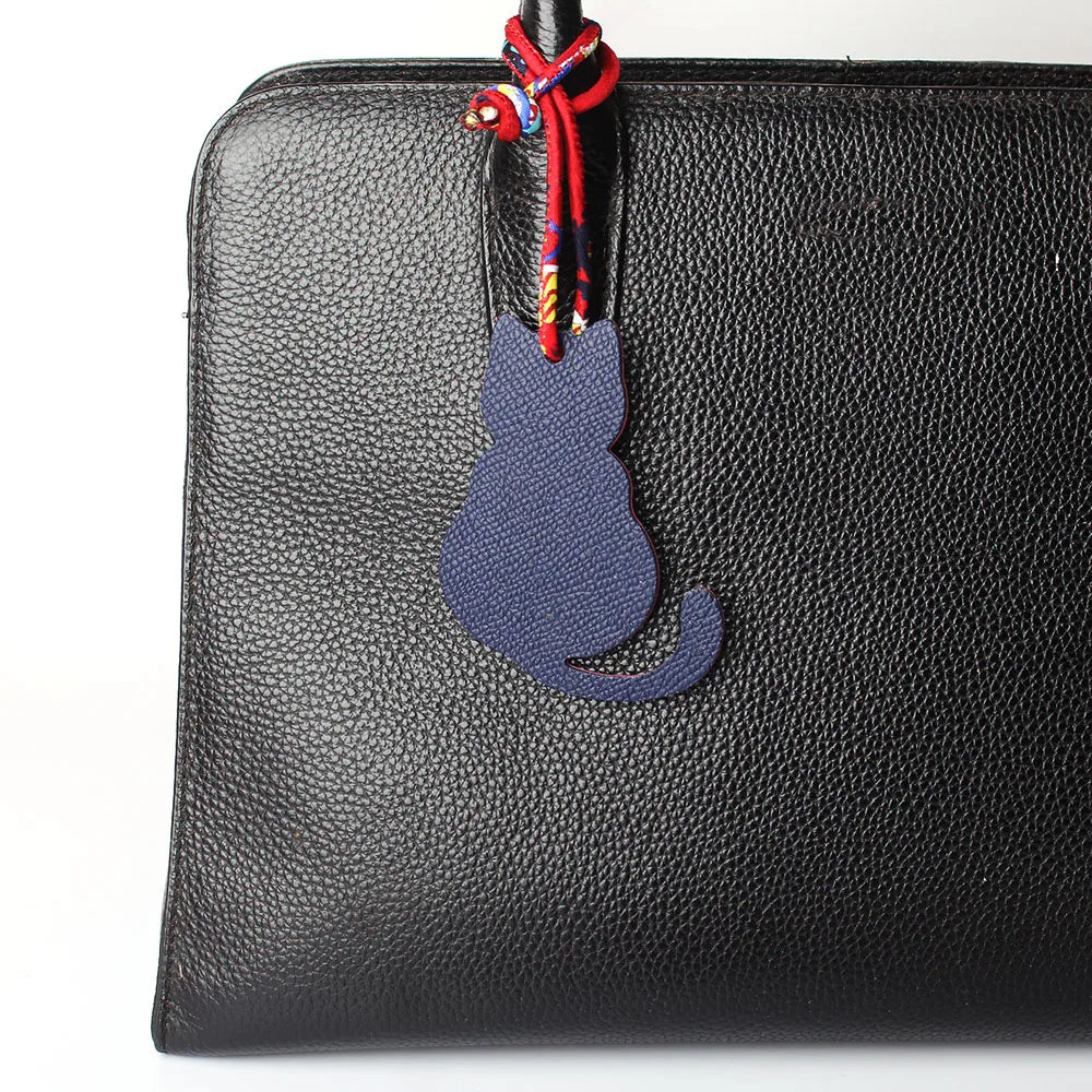 Llavero de piel de cocodrilo para mujer con figura de gato sobre un bolso negro de cuero auténtico.